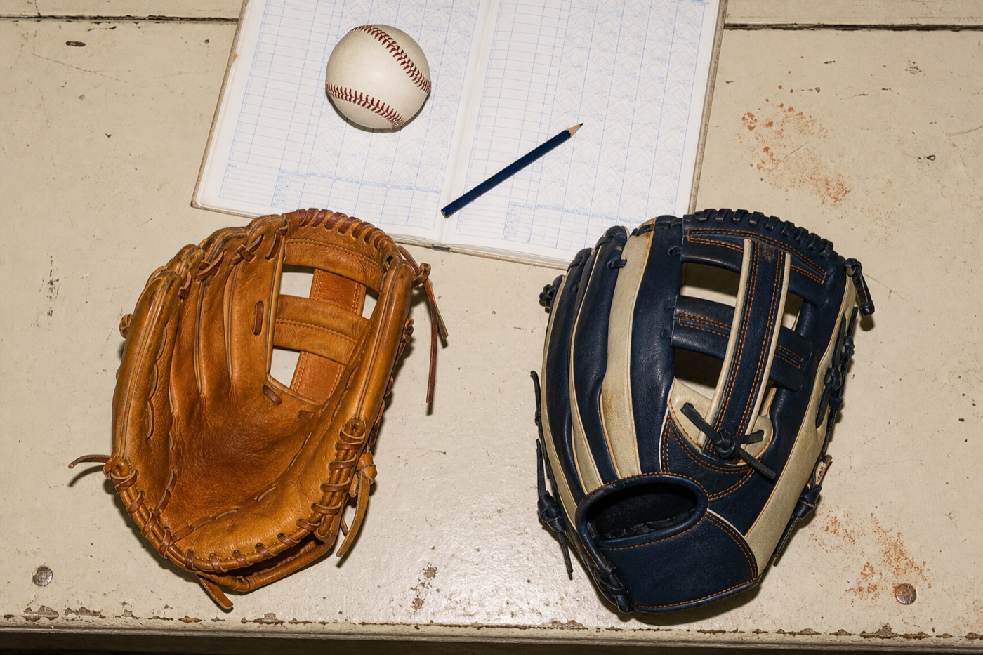 Two youth baseball fielding gloves beside a scorebook